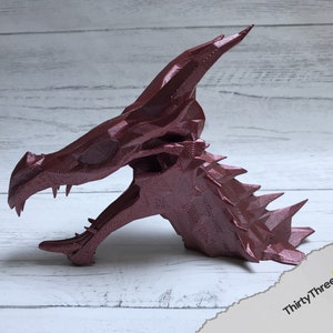 May include: A 3D printed dragon head sculpture in a deep burgundy red color. The sculpture is detailed with sharp teeth and scales.