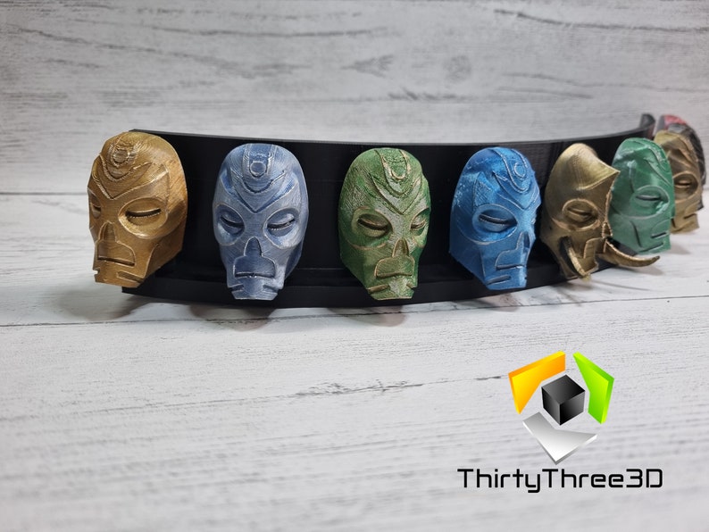 May include: A set of seven 3D printed masks, each with a unique design and color. The masks are arranged in a row on a black display stand. The masks are made of a smooth, plastic-like material and have a variety of colors, including gold, blue, green, and brown.