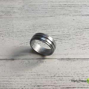 May include: A silver ring with two grooves around the band.