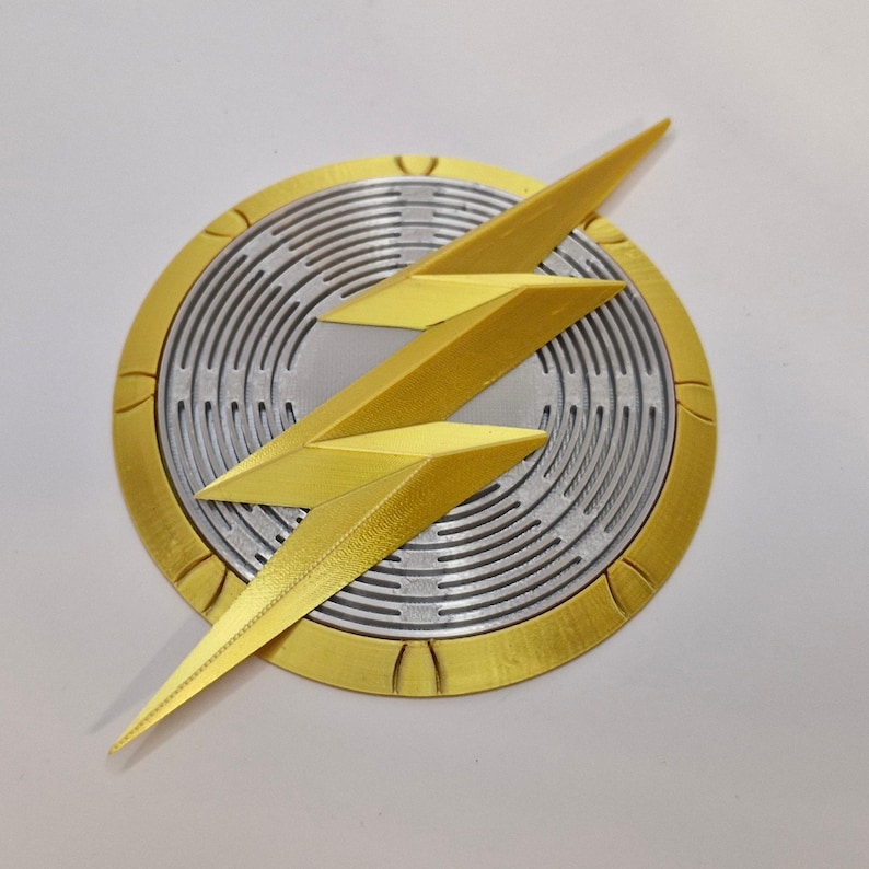 Puede incluir: Un emblema dorado y plateado con un dise&ntilde;o de rayo. El rayo es dorado y est&aacute; posicionado sobre un fondo circular plateado con detalles de c&iacute;rculos conc&eacute;ntricos. El borde exterior del c&iacute;rculo es dorado.