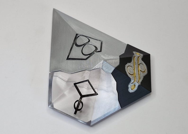 May include: Abstract geometric art piece with a multifaceted design. The artwork features a combination of silver, black, and clear acrylic elements. Black line art symbols are incorporated into the design, adding visual interest.