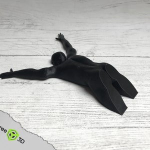May include: A black 3D printed doorstop shaped like a person lying on their stomach with arms outstretched.