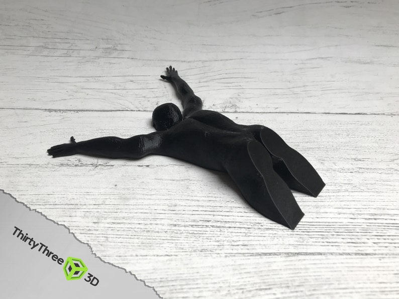May include: A black 3D printed doorstop shaped like a person lying on their stomach with arms outstretched.