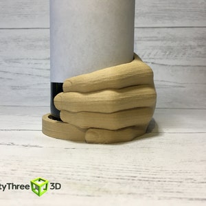 May include: A wooden hand-shaped bottle holder, holding a wine bottle with a white label. The holder is made of light brown wood and has a natural wood finish.