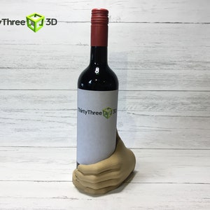 May include: A brown hand-shaped wine bottle holder with a bottle of red wine inside. The bottle has a white label with the text "ThirtyThree 3D".