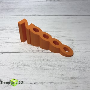 May include: Orange plastic doorstop shaped like the number 10000. The doorstop is on a white wooden surface.