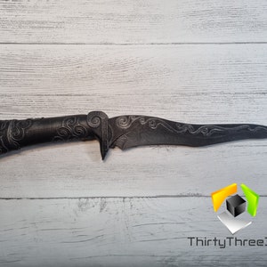 May include: A black, intricately carved dagger with a curved blade and a detailed handle. The dagger is lying on a white wooden surface. The text "ThirtyThree3D" is visible in the lower right corner of the image.