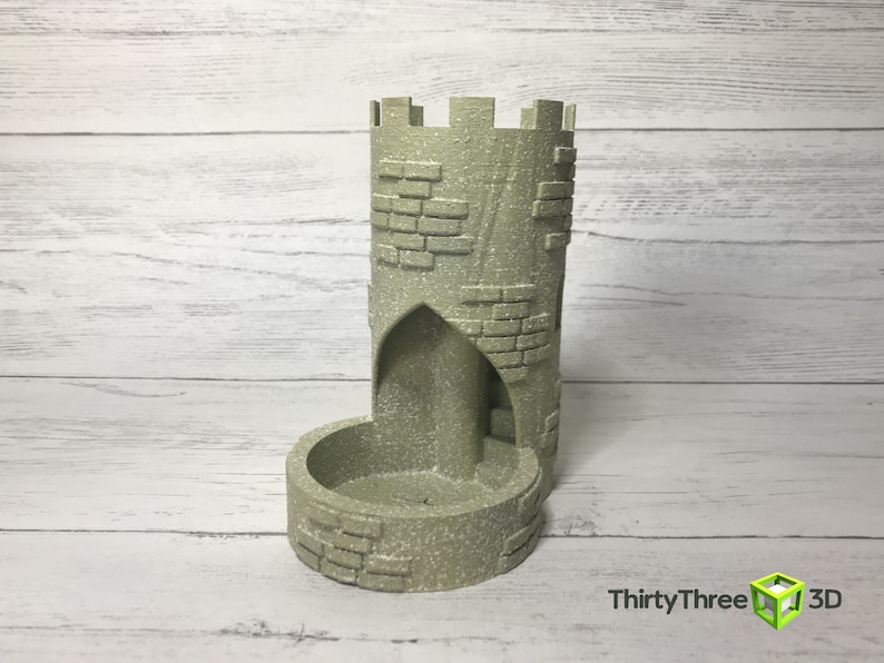 May include: A gray stone tower-shaped dice rolling tower with a brick pattern. The tower has a small opening at the top and a larger opening at the bottom for dice to roll through.