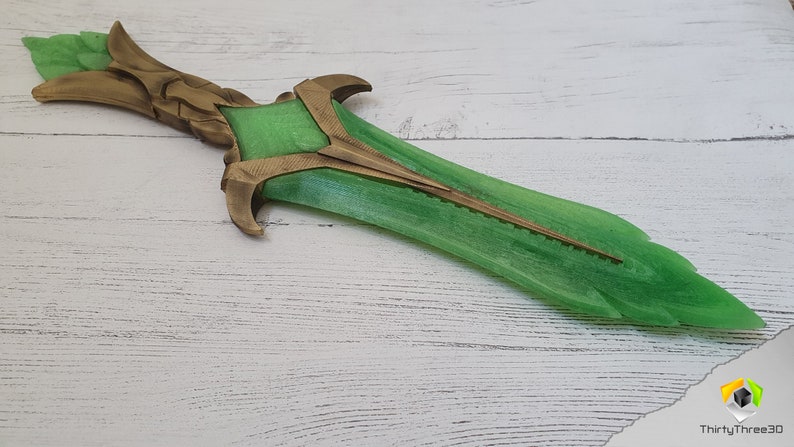 May include: A green and gold decorative sword with a detailed hilt and a sharp point. The sword is made of a translucent material and has a metallic sheen.