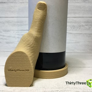 May include: A 3D printed wooden hand holding a wine bottle. The hand is giving a thumbs up and has the text "ThirtyThree3D" printed on the palm. The bottle is sitting on a wooden coaster.