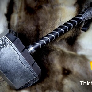 May include: A silver-colored hammer with a black and silver handle. The hammer has a detailed design on the head and a textured surface. The hammer is resting on a furry surface.