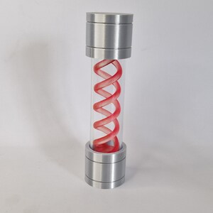 May include: A cylindrical container with a clear glass tube and metallic silver caps at the top and bottom. Inside, a vibrant red, double-helix structure is visible, creating a striking visual contrast. The design suggests a science fiction or laboratory theme.