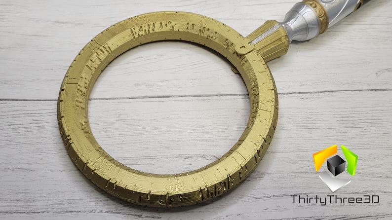 Pode incluir: Um anel dourado com detalhes intrincados e uma al&ccedil;a prateada. O anel &eacute; circular e tem uma superf&iacute;cie texturizada.