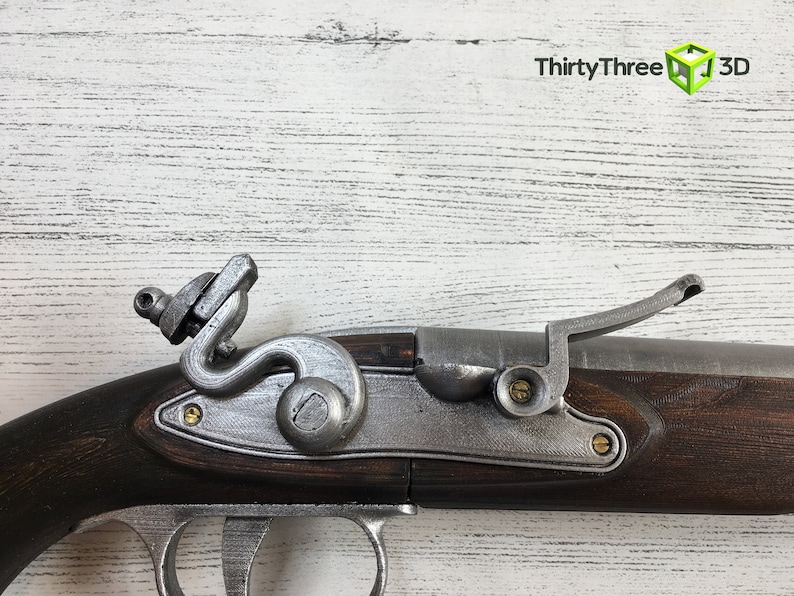 Puede incluir: Vista detallada de una r&eacute;plica de pistola de chispa. La pistola presenta una culata de madera marr&oacute;n oscuro, componentes met&aacute;licos de color plateado y detalles en color lat&oacute;n. El gatillo, el martillo y otros mecanismos son claramente visibles, mostrando el intrincado dise&ntilde;o.