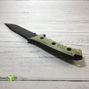 May include: A black and green tactical knife with a serrated blade and a textured handle. The handle has multiple black screws.