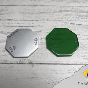 May include: Two octagonal shaped bases, one silver and one green. The bases are made of a smooth, hard material. The silver base has the text "SILICONE GEL" printed on it.