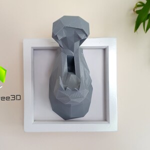 May include: A gray, geometric, 3D printed hippopotamus head mounted in a white frame. The hippopotamus head is a wall decor piece.