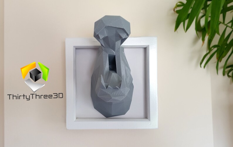 May include: A gray, geometric, 3D printed hippopotamus head mounted in a white frame. The hippopotamus head is a wall decor piece.