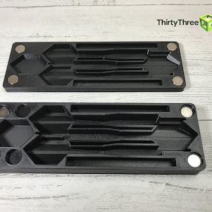 May include: Two black plastic trays with multiple compartments for holding tools or other small items. The trays have magnets on the sides and are designed to be stacked together.
