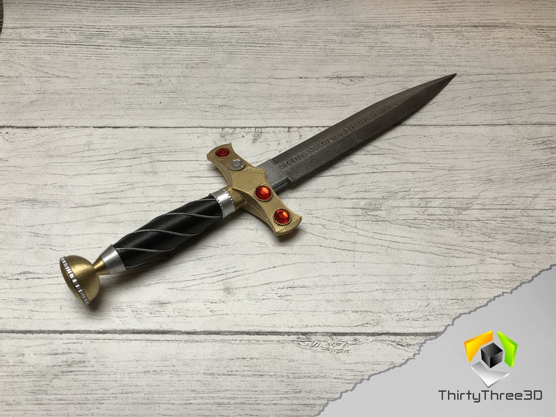 May include: A gold and silver dagger with a black handle and red gems. The blade is engraved with the words "SIC SEMPER TYRANNIS".