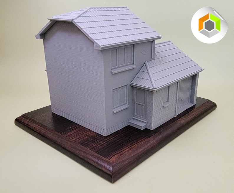 May include: A gray 3D printed model of a house on a dark wood base. The house has a garage and a small front porch.