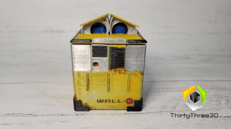 May include: A yellow and silver WALL-E robot toy with a rusty appearance. The robot has a rectangular body with a small, rectangular window on the front. The robot's eyes are blue and the text "WALL-E" is printed on the front of the robot.