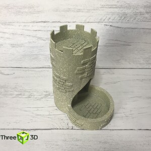 May include: A beige, 3D printed tower-shaped dice rolling tray with a textured brick pattern. The tower has a crenellated top and a curved opening for dice to roll out.