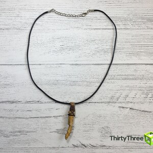 May include: A black cord necklace with a brown and beige bone pendant. The pendant is shaped like a tooth.