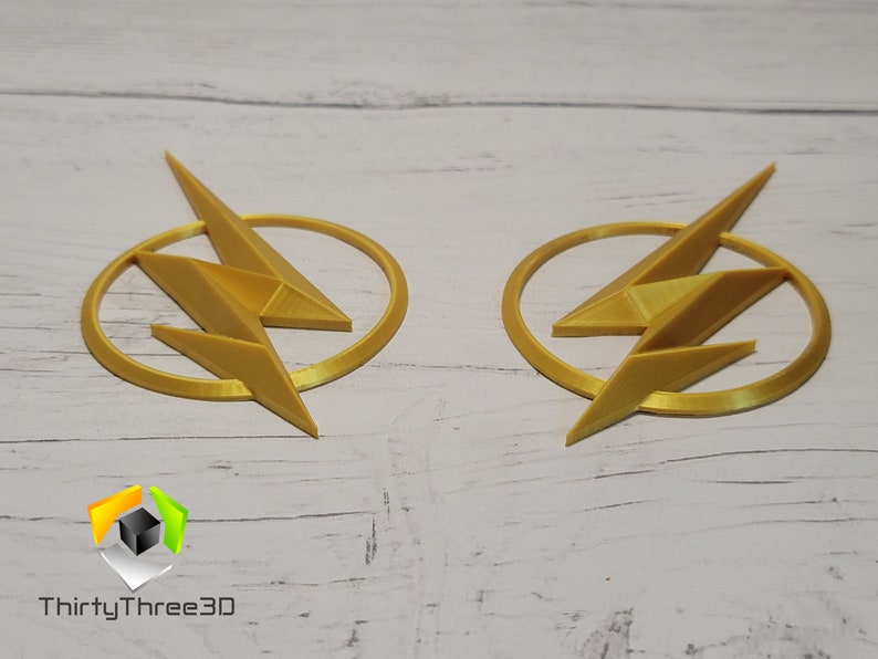 May include: Two gold-colored 3D printed Flash logos. Each logo features a lightning bolt inside a circle.