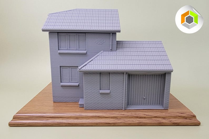 May include: A gray 3D printed model of a two-story house with a garage. The house is on a wooden base.