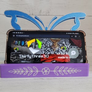 Peut inclure: Un support de t&eacute;l&eacute;phone violet avec un motif floral et un support de t&eacute;l&eacute;phone en forme de papillon bleu. Le support de t&eacute;l&eacute;phone est en bois et poss&egrave;de une fente pour un t&eacute;l&eacute;phone. Le support de t&eacute;l&eacute;phone est en plastique et a un design de papillon. Le support de t&eacute;l&eacute;phone est un excellent moyen de garder votre t&eacute;l&eacute;phone debout et facilement accessible.
