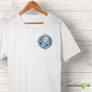 May include: White t-shirt with a blue and silver circular design featuring a stylized eye and runes. The design is centered on the shirt.