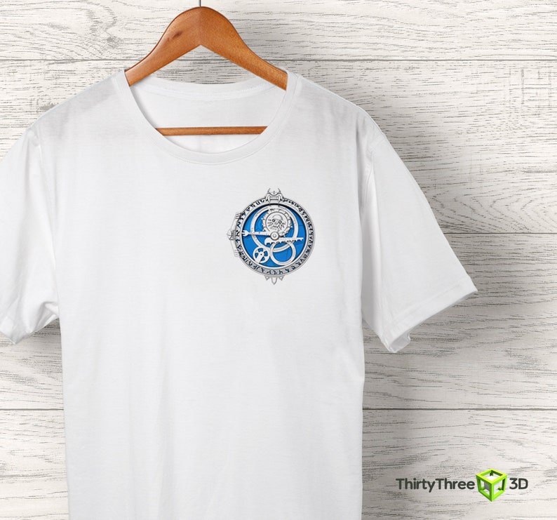 May include: White t-shirt with a blue and silver circular design featuring a stylized eye and runes. The design is centered on the shirt.