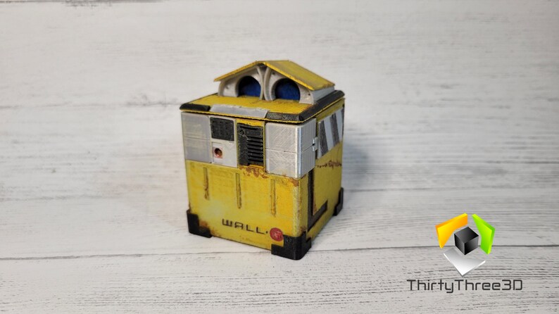 May include: A yellow and gray WALL-E robot toy with a white roof and blue eyes. The robot is made of wood and has a weathered look.