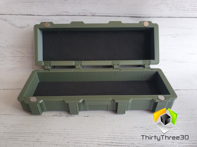 May include: A green rectangular storage box with a hinged lid and magnetic closures. The box is lined with black foam.