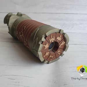 May include: A brown and green wooden kaleidoscope with a circular viewing end. The end is decorated with a brown circle with various symbols and designs.