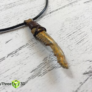 May include: A gold-colored pendant necklace with a bone-shaped charm wrapped in brown leather cord. The necklace is on a black cord.