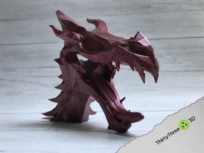 May include: A 3D printed dragon head sculpture in a deep burgundy red color. The sculpture is detailed with sharp teeth and scales.