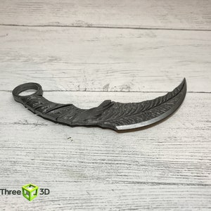 May include: A silver-colored, curved, metal knife with a decorative pattern on the blade. The knife has a ring at the top of the handle.