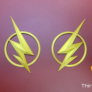 Op de afbeelding: Twee goudkleurige The Flash-logo's met een bliksemontwerp. De logo's bevinden zich op een rode achtergrond.