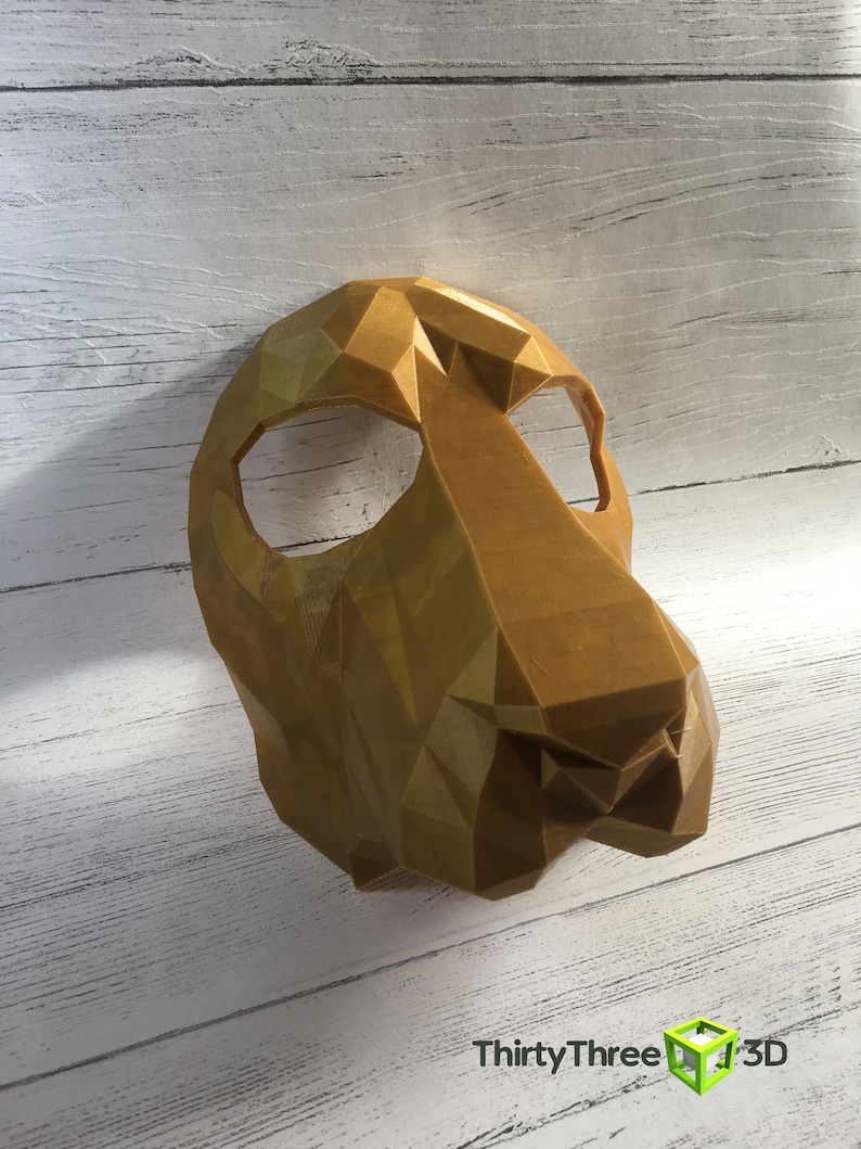 May include: A gold-colored, geometric, 3D printed animal mask. The mask has a triangular shape and is designed to cover the eyes and nose.