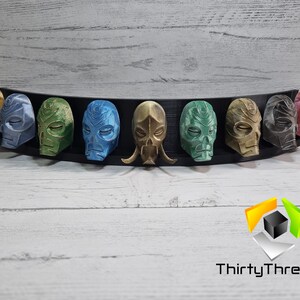 May include: A set of eight 3D printed masks, each with a unique design and color. The masks are displayed on a black curved stand. The masks are painted in various colors, including gold, green, blue, and red.