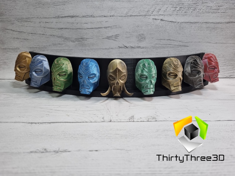 May include: A set of eight 3D printed masks, each with a unique design and color. The masks are displayed on a black curved stand. The masks are painted in various colors, including gold, green, blue, and red.