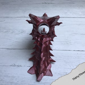 May include: A 3D printed, burgundy-colored, dragon-shaped object with a white, circular opening in the center of its head.