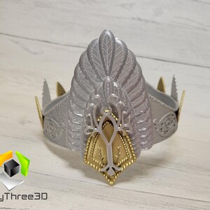 以下が含まれることがあります： 中央に金色のデザインが施された銀色の王冠。王冠は頂上に羽根のデザインがあり、基部には細かい模様が施されています。