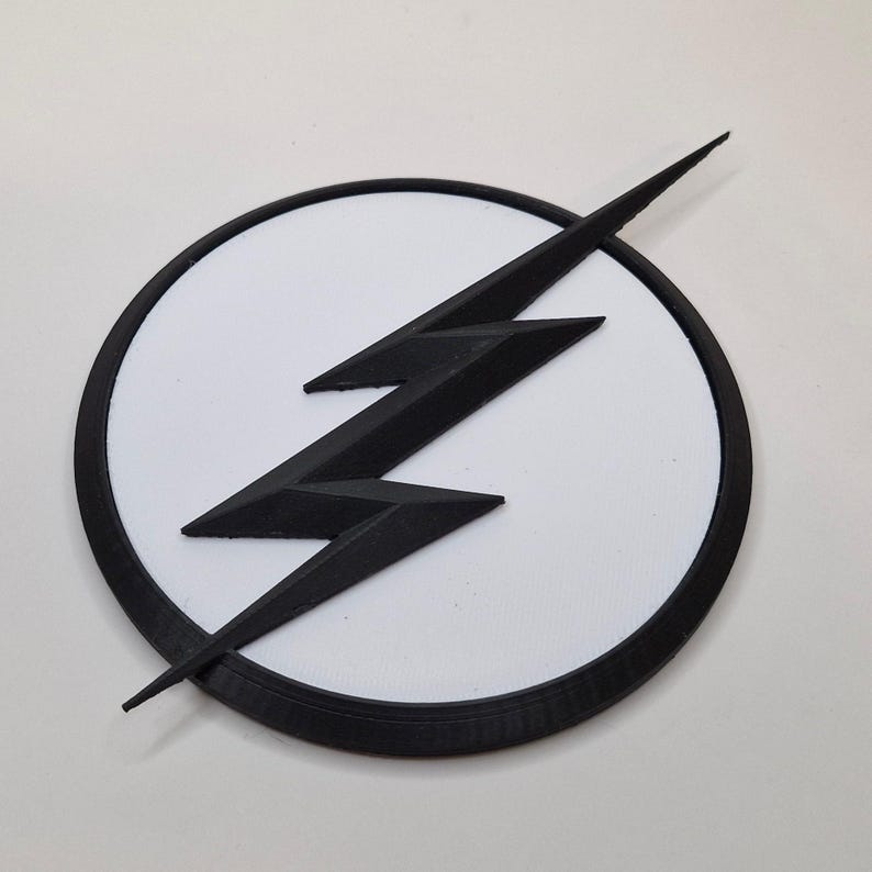 May include: A black lightning bolt emblem on a white circle, set against a white background. The emblem has a black border. The lightning bolt is a stylized, three-pronged design.