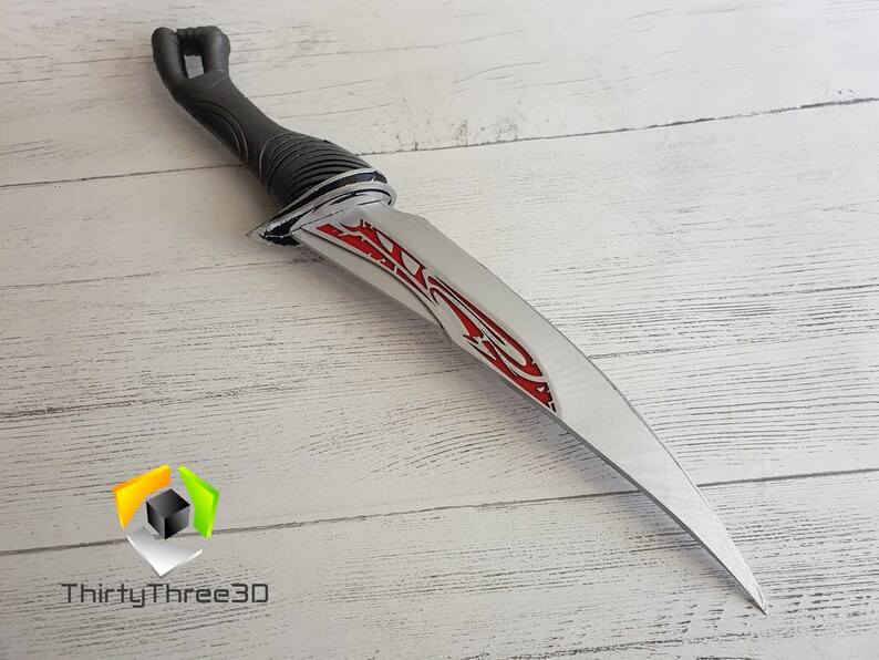 May include: A silver dagger with a black handle and red accents. The blade has a decorative design with a sharp point.