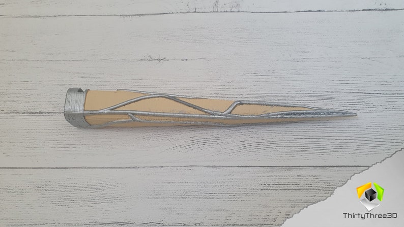 Op de afbeelding: Een zilveren en beige 3D-geprint rekwisiet dat lijkt op een skeletachtige arm, met een puntig uiteinde.