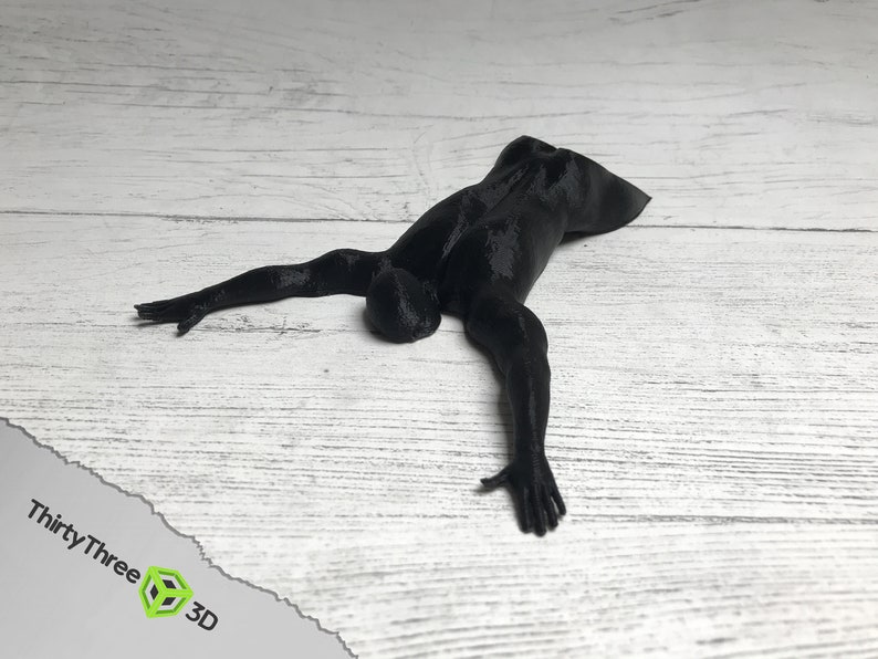 May include: A black 3D printed figurine of a person lying on their stomach with arms outstretched.