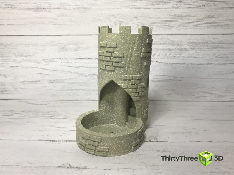 May include: A gray stone tower-shaped dice rolling tower with a brick pattern. The tower has a small opening at the top and a larger opening at the bottom for dice to roll through.